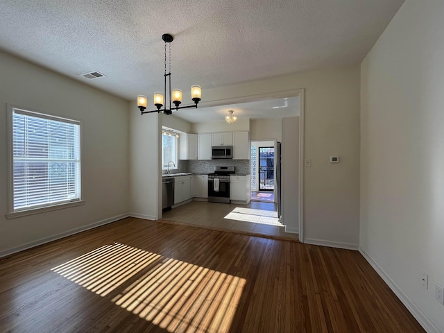 kitchen featuring tasteful backsplash, decorative light fixtures, white cabinetry, stainless steel appliances, and a chandelier