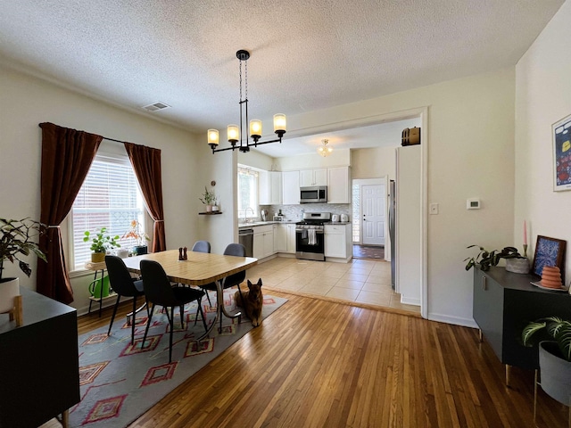 dining area with light hardwood / wood-style flooring, sink, a textured ceiling, and a chandelier