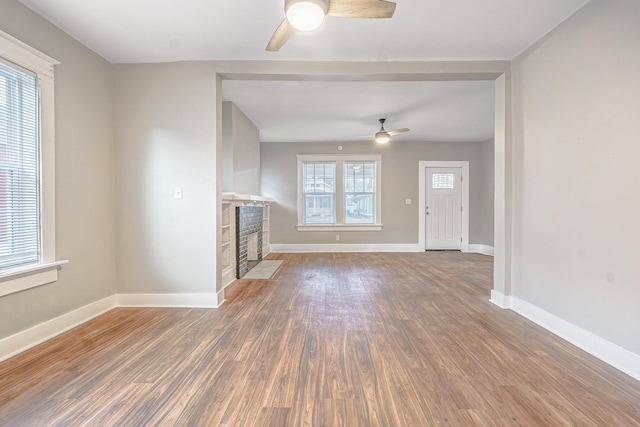 unfurnished living room featuring a fireplace, wood-type flooring, and a wealth of natural light