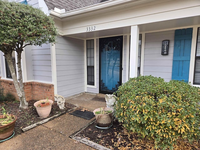 entrance to property with a shingled roof and brick siding