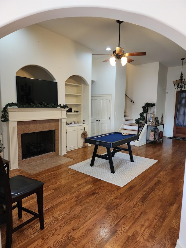 playroom with ceiling fan with notable chandelier, wood-type flooring, built in features, and a fireplace