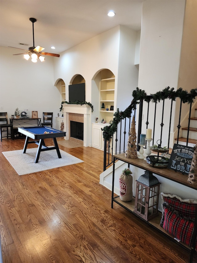 rec room with built in shelves, ceiling fan, a fireplace, and wood-type flooring