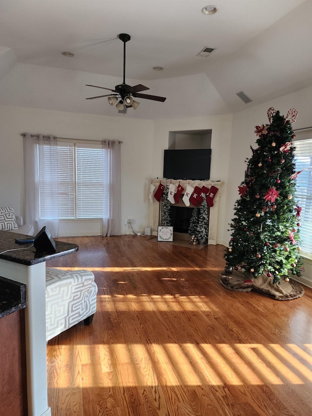 living room with wood-type flooring, vaulted ceiling, ceiling fan, and a tiled fireplace