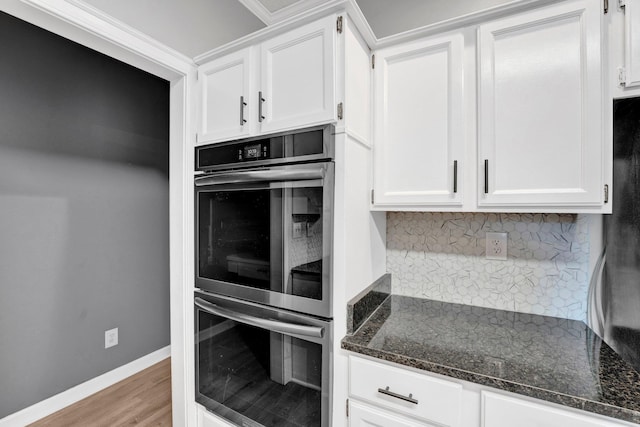 kitchen featuring dark stone counters, crown molding, tasteful backsplash, white cabinetry, and stainless steel double oven