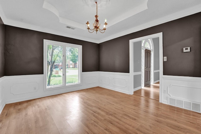 empty room with a notable chandelier, a raised ceiling, and light hardwood / wood-style flooring