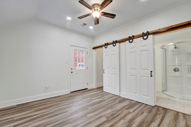 unfurnished bedroom with a barn door, ceiling fan, light hardwood / wood-style floors, and ornamental molding