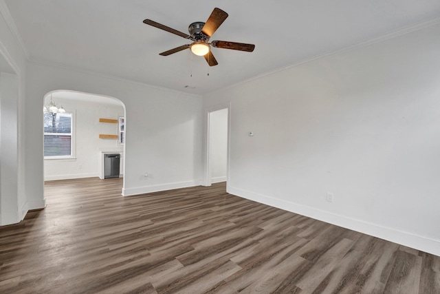 empty room featuring ceiling fan with notable chandelier, crown molding, and dark wood-type flooring