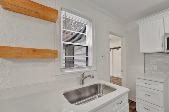 kitchen featuring backsplash, sink, white cabinetry, and ornamental molding