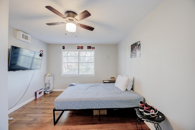 bedroom with ceiling fan, wood-type flooring, and a textured ceiling