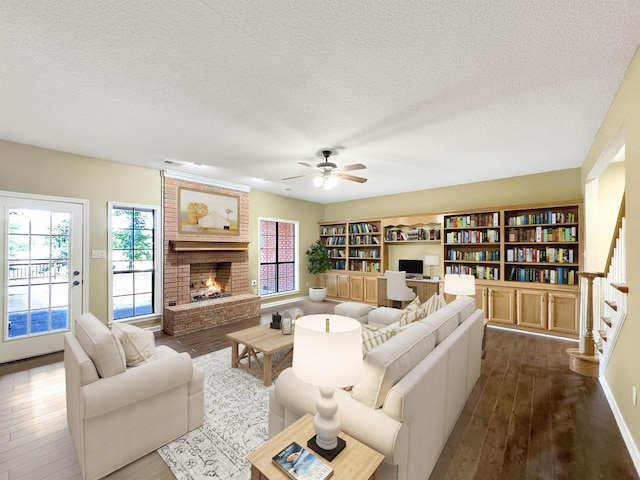 living room with ceiling fan, a fireplace, dark wood-type flooring, and a textured ceiling