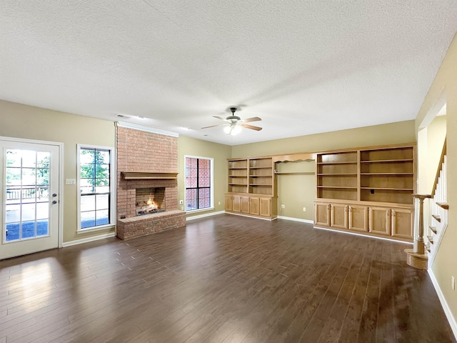 unfurnished living room featuring a textured ceiling, a brick fireplace, ceiling fan, and dark wood-type flooring