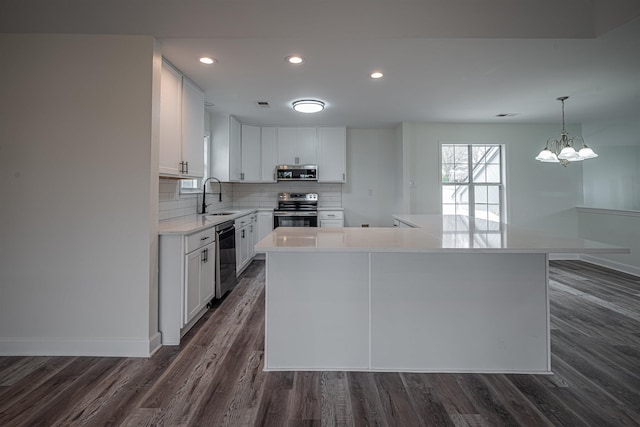 kitchen featuring appliances with stainless steel finishes, sink, a notable chandelier, a center island, and white cabinetry