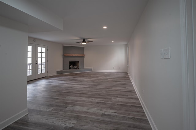 unfurnished living room featuring a brick fireplace, ceiling fan, dark wood-type flooring, and french doors