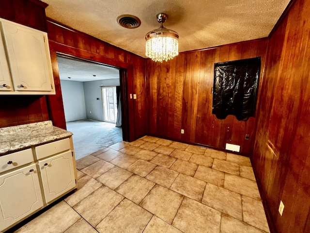 unfurnished dining area with visible vents, light colored carpet, a textured ceiling, wood walls, and a chandelier