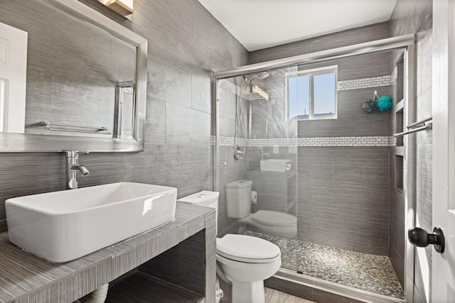 bathroom with an enclosed shower, toilet, sink, and tile walls