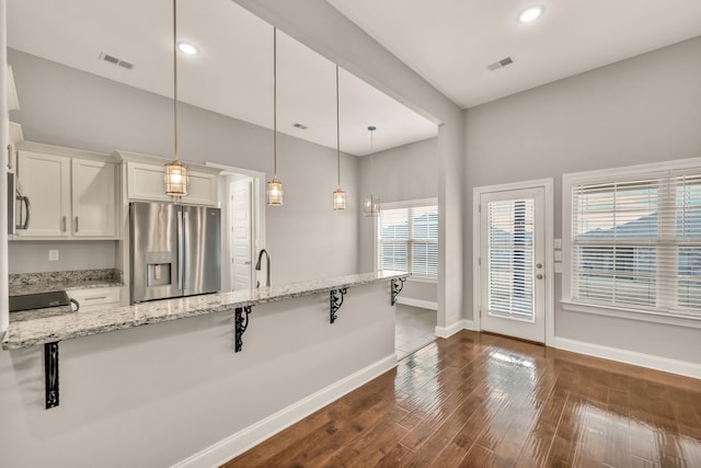 kitchen with a kitchen breakfast bar, stainless steel fridge, light stone countertops, decorative light fixtures, and white cabinetry