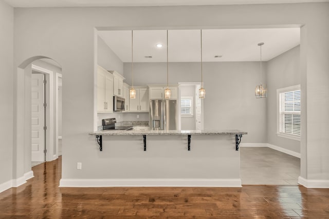 kitchen featuring a kitchen bar, hanging light fixtures, white cabinets, and stainless steel appliances