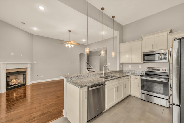 kitchen with light stone counters, stainless steel appliances, ceiling fan, sink, and white cabinetry