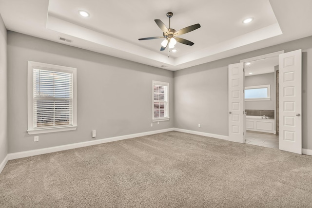 unfurnished bedroom with light carpet, a tray ceiling, and ceiling fan