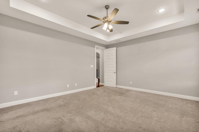 carpeted spare room with ceiling fan and a raised ceiling