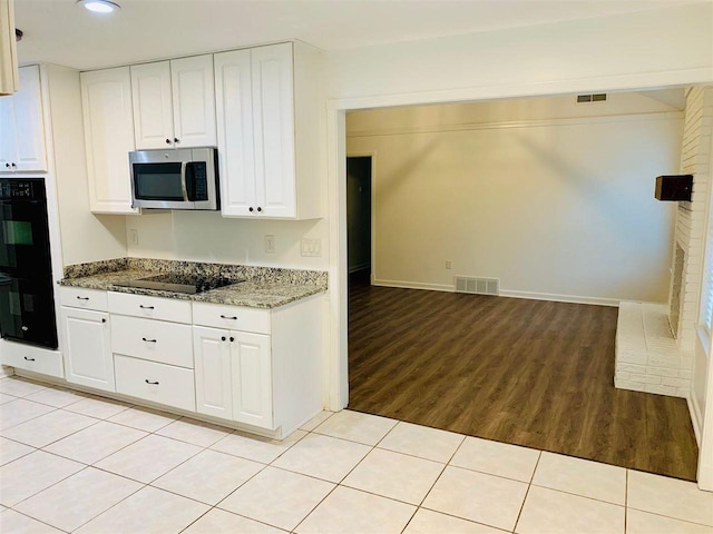 kitchen featuring stone counters, white cabinetry, light tile patterned floors, and black appliances