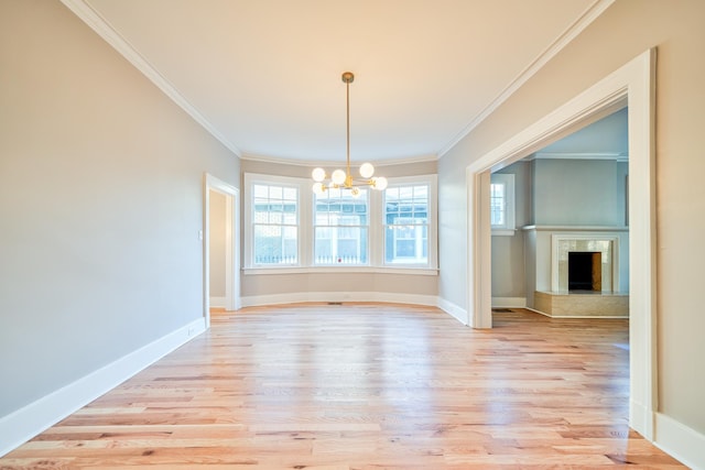 unfurnished dining area with crown molding, a fireplace, a chandelier, and light hardwood / wood-style flooring