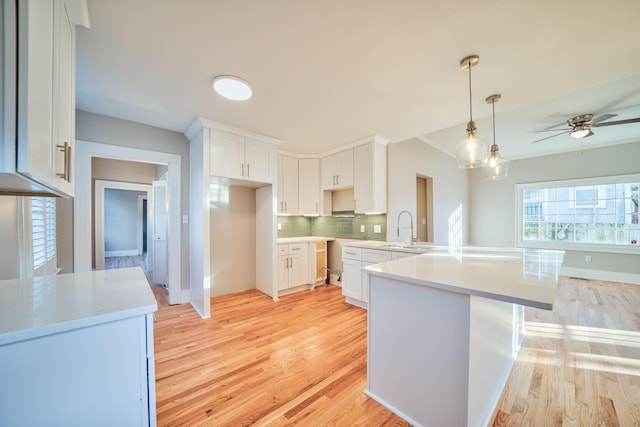 kitchen featuring decorative backsplash, white cabinetry, hanging light fixtures, and light hardwood / wood-style flooring