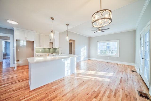 kitchen featuring white cabinets, ceiling fan with notable chandelier, crown molding, light hardwood / wood-style flooring, and decorative backsplash