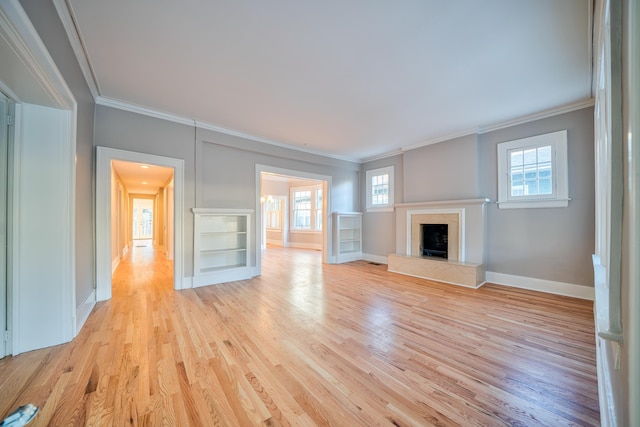 unfurnished living room featuring light hardwood / wood-style floors, built in shelves, a healthy amount of sunlight, and ornamental molding