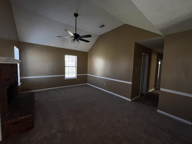 unfurnished living room featuring dark carpet, lofted ceiling, ceiling fan, a fireplace, and a textured ceiling