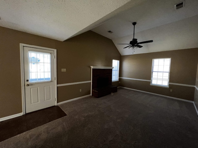 unfurnished living room with ceiling fan, dark colored carpet, a brick fireplace, a textured ceiling, and lofted ceiling