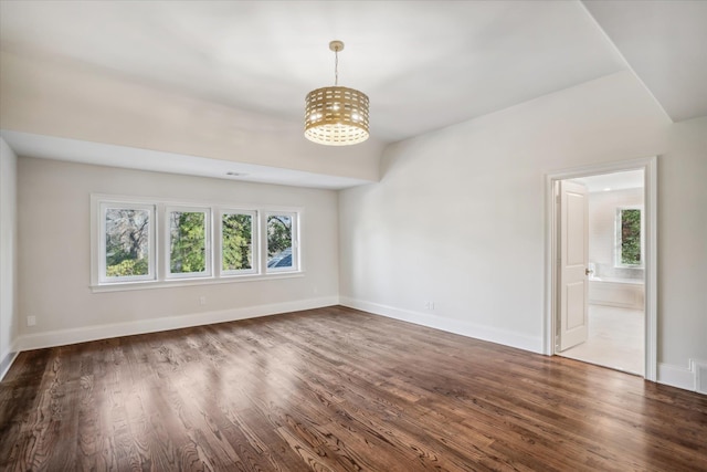 empty room with dark hardwood / wood-style floors, a wealth of natural light, and a chandelier