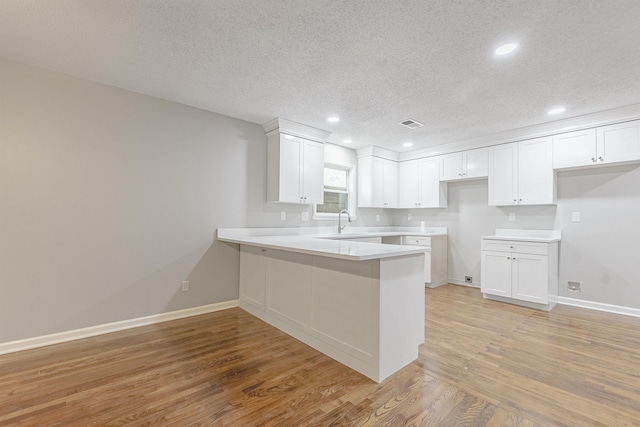 kitchen featuring white cabinetry, sink, kitchen peninsula, light hardwood / wood-style floors, and a textured ceiling