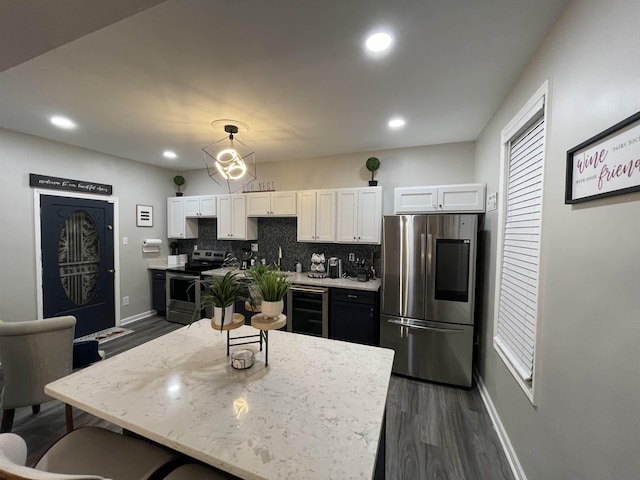 kitchen with hanging light fixtures, decorative backsplash, appliances with stainless steel finishes, white cabinetry, and beverage cooler