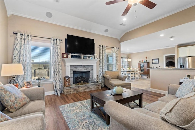 living room with ceiling fan, crown molding, wood-type flooring, a stone fireplace, and lofted ceiling