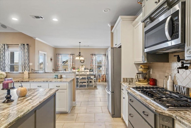 kitchen featuring a wealth of natural light, white cabinets, decorative light fixtures, and appliances with stainless steel finishes