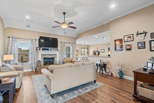 living room featuring crown molding, a fireplace, ceiling fan with notable chandelier, and light hardwood / wood-style flooring