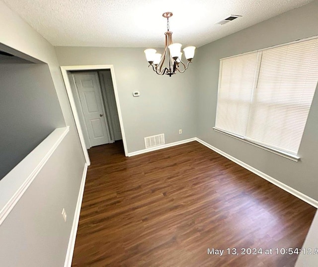 unfurnished dining area with dark wood-type flooring, a textured ceiling, and an inviting chandelier