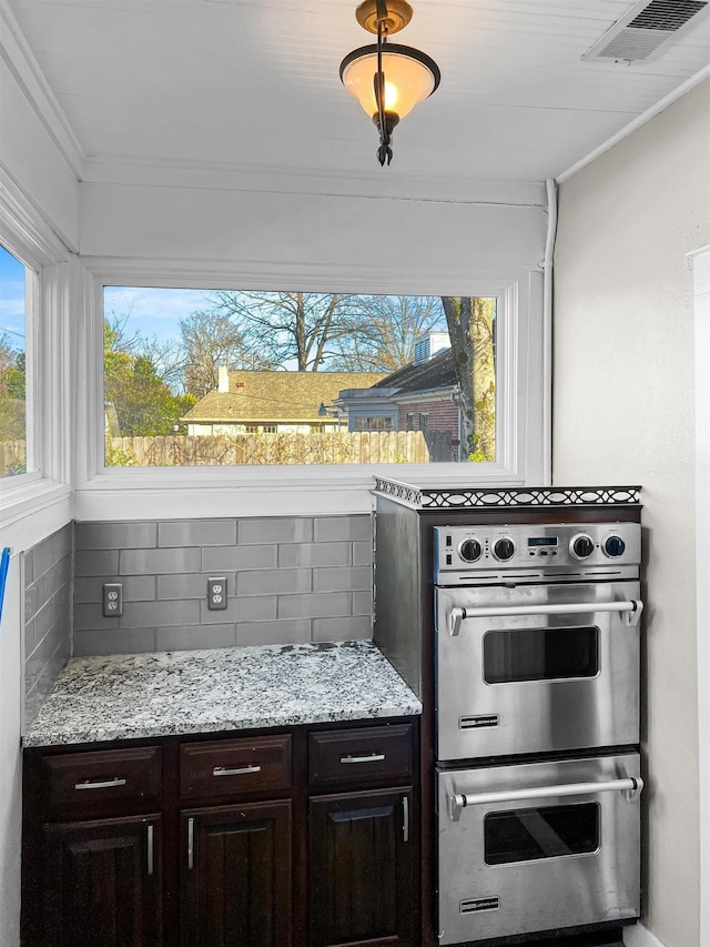 kitchen featuring dark brown cabinetry, stainless steel double oven, crown molding, and tasteful backsplash