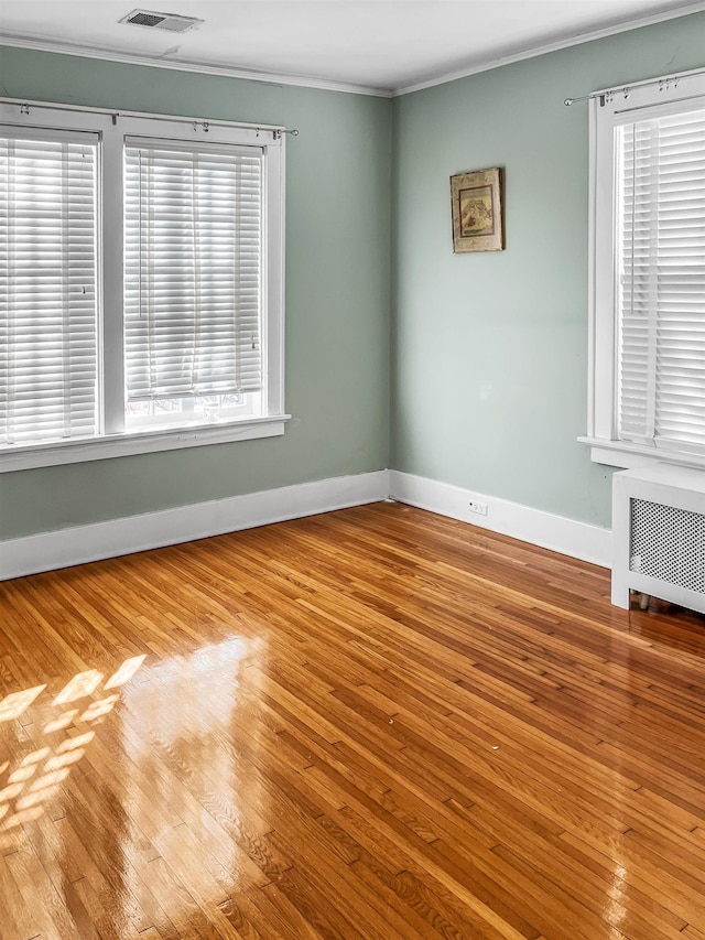 empty room with plenty of natural light, ornamental molding, radiator, and light hardwood / wood-style flooring