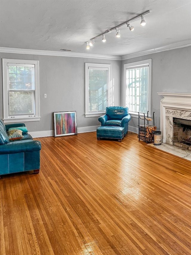 living room featuring plenty of natural light, light wood-type flooring, ornamental molding, and a high end fireplace