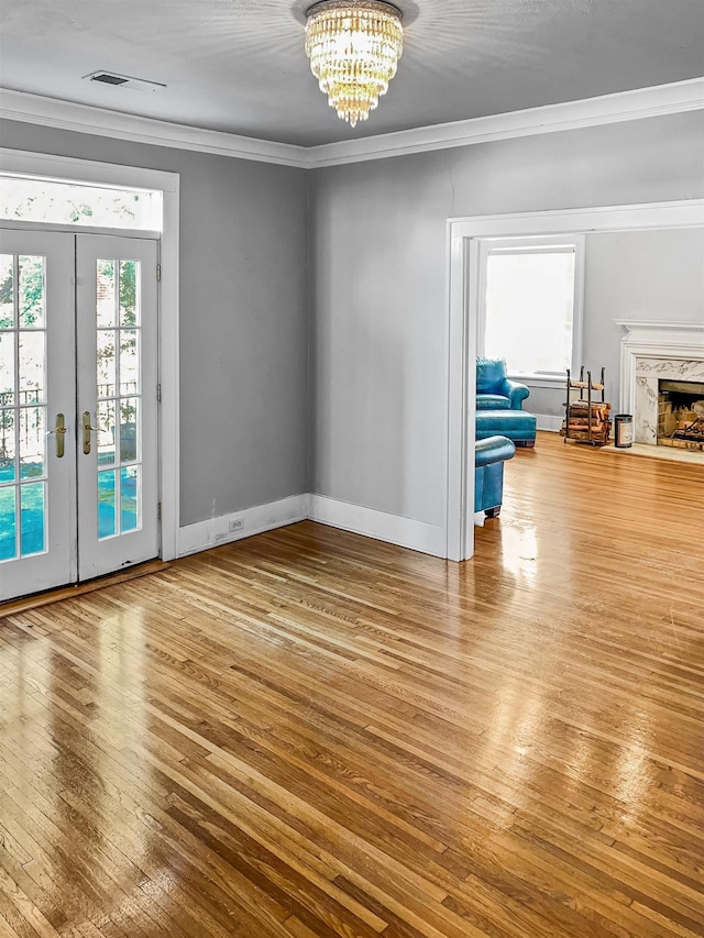 empty room featuring french doors, crown molding, a notable chandelier, a premium fireplace, and hardwood / wood-style floors