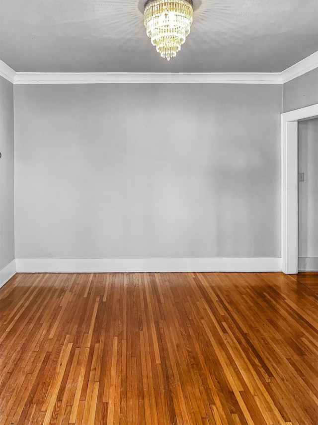 empty room with crown molding, hardwood / wood-style flooring, and a notable chandelier