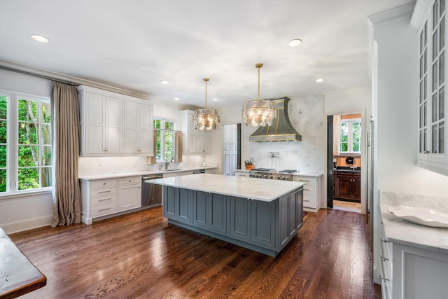 kitchen featuring dishwasher, wall chimney exhaust hood, hanging light fixtures, a kitchen island, and white cabinets