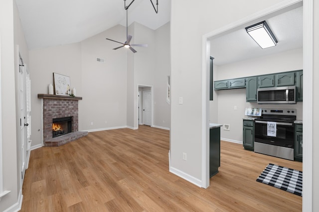 kitchen featuring appliances with stainless steel finishes, ceiling fan, high vaulted ceiling, light hardwood / wood-style flooring, and a fireplace