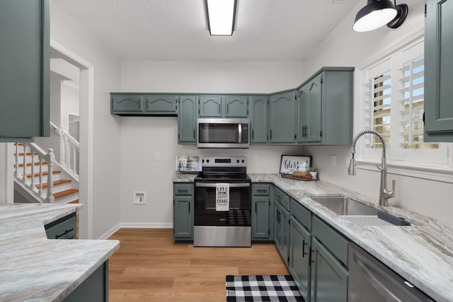 kitchen featuring sink, light hardwood / wood-style flooring, a textured ceiling, light stone counters, and stainless steel appliances