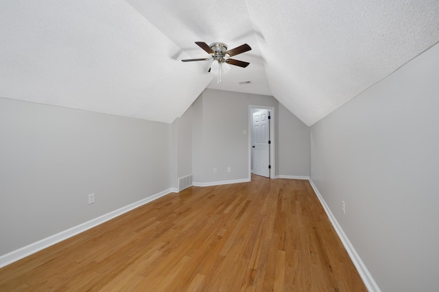 additional living space featuring a textured ceiling, ceiling fan, vaulted ceiling, and light wood-type flooring