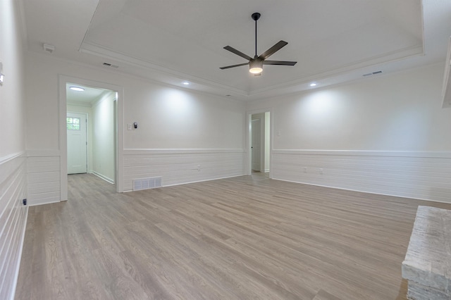 spare room with light wood-type flooring, a raised ceiling, ceiling fan, and crown molding