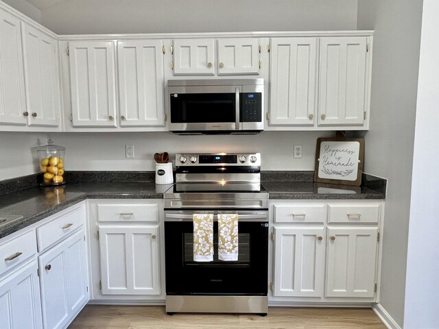 kitchen featuring appliances with stainless steel finishes, light wood-type flooring, white cabinetry, and dark stone counters