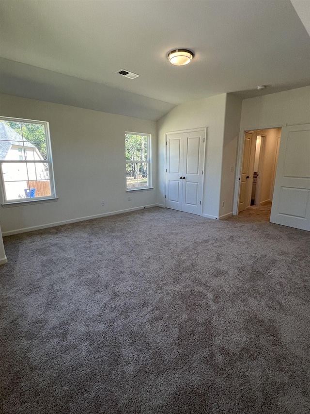 unfurnished bedroom with carpet flooring, multiple windows, and vaulted ceiling